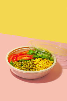 High angle of salad bowl with slices of tomato, spinach leaves, corn kernels and peas placed on pink surface against yellow wall - ADSF46663
