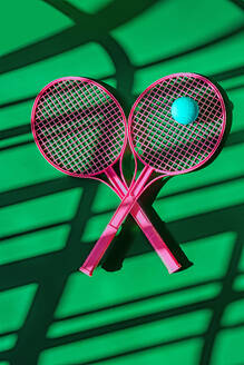 Top view of creative design of pink tennis rackets and blue ball against green sports ground with shadows in daylight - ADSF46675