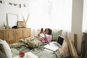 Teenager-Mädchen mit Smartphone auf dem Bett liegend zu Hause - ALKF00545