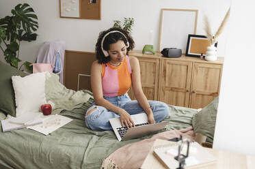 Smiling teenage girl using laptop on bed at home - ALKF00553