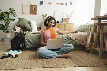 Happy teenage girl wearing wireless headphones talking on video call - ALKF00554