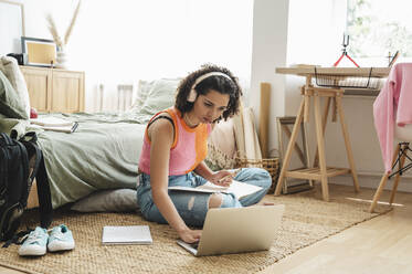 Curly haired teenage girl using laptop and doing homework at home - ALKF00559