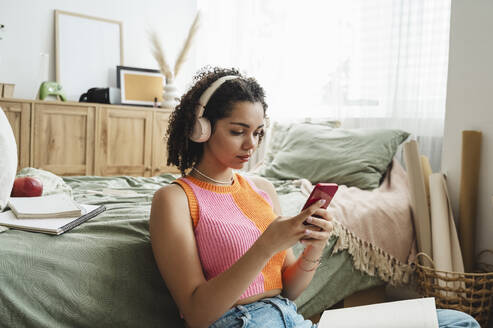 Teenager-Mädchen mit drahtlosen Kopfhörern und Mobiltelefon auf dem Teppich zu Hause - ALKF00566