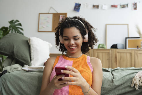 Happy teenage girl using mobile phone in bedroom - ALKF00567