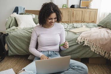 Happy curly haired girl making payment through credit card at home - ALKF00576