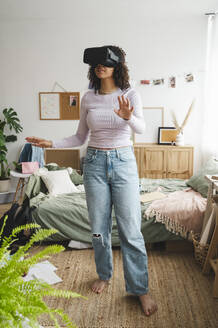 Mädchen trägt Virtual-Reality-Simulatoren und gestikuliert zu Hause - ALKF00583