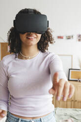 Smiling girl wearing virtual reality simulators gesturing at home - ALKF00584