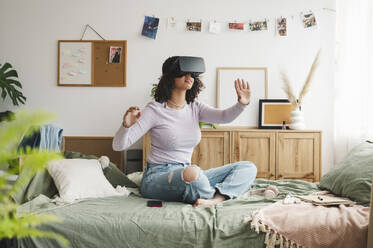 Mädchen trägt Virtual-Reality-Simulatoren und gestikuliert auf dem Bett zu Hause - ALKF00587