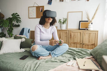 Girl wearing virtual reality simulators holding game controller on bed at home - ALKF00591