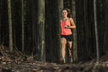 Lächelnde junge Sportlerin beim Joggen im Wald - STSF03749