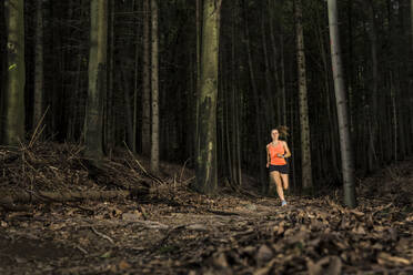 Dedicated sportswoman running amidst tree trunks in forest - STSF03750