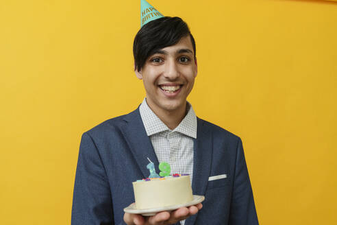 Smiling man holding cake against yellow background - OSF02035