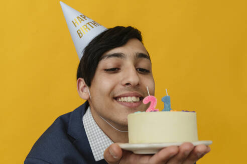 Happy man with party hat looking at 21st birthday cake - OSF02037