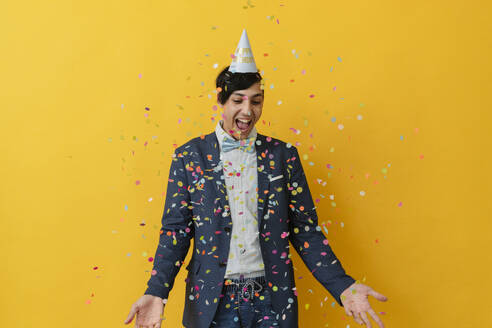 Cheerful man enjoying with confetti against yellow background - OSF02047