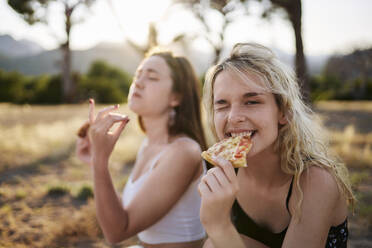 Junge Frau zwinkert und isst Pizza mit Freund im Hintergrund - ANNF00358