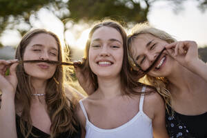 Lächelnde Frauen spielen am Wochenende im Park mit den Haaren ihrer Freundin - ANNF00371