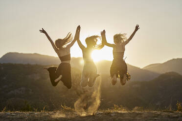 Cheerful friends holding hands and jumping at sunset - ANNF00376