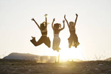 Frauen springen mit erhobenen Händen und genießen den Sonnenuntergang - ANNF00377