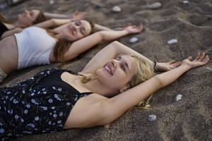 Glückliche Frau, die im Urlaub bei Freunden im Sand liegt - ANNF00383