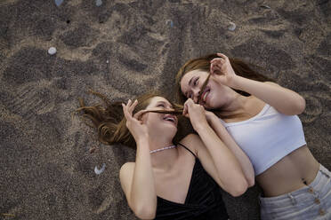 Glückliche Frauen machen Schnurrbart mit Haaren und liegen auf Sand - ANNF00384