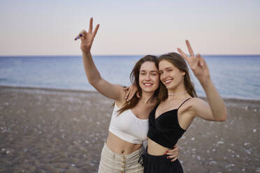 Glückliche Freunde gestikulieren am Strand im Urlaub das Friedenszeichen - ANNF00388