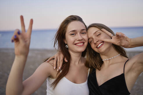 Glückliche junge Freunde, die am Strand ein Friedenszeichen machen - ANNF00389