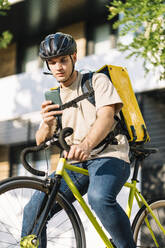 Zusteller, der ein Mobiltelefon benutzt und mit einer Tasche auf dem Fahrrad sitzt - DAMF01219