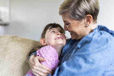 Glückliche Mutter, die ihre Tochter auf dem Sofa sitzend umarmt - WPEF07568