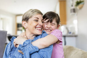 Lächelnde Mutter und Tochter mit geschlossenen Augen, die sich zu Hause umarmen - WPEF07571