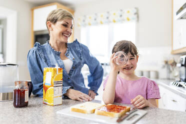 Verspieltes Mädchen schaut in der Küche durch ein Trinkglas der Mutter - WPEF07580