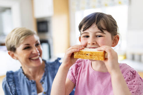 Mädchen, das von seiner Mutter zu Hause ein Sandwich isst - WPEF07582