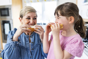 Mutter und Tochter essen Sandwiches in der Küche - WPEF07583