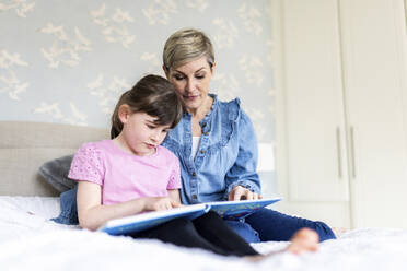 Daughter reading picture book with mother in bedroom - WPEF07584