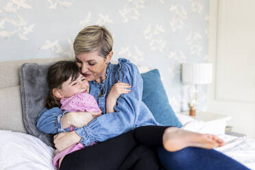 Mother hugging daughter lying on bed at home - WPEF07585