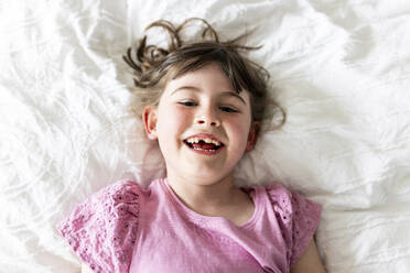 Glückliches Mädchen auf dem Bett liegend im Schlafzimmer zu Hause - WPEF07595