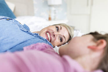 Lächelnde Mutter liegt mit ihrer Tochter auf dem Bett im Schlafzimmer - WPEF07598
