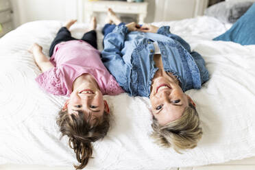 Happy mother and daughter lying on bed at home - WPEF07600