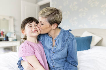 Mutter küsst lächelnde Tochter im Schlafzimmer - WPEF07601