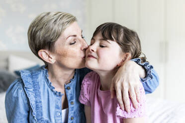 Mature mother kissing daughter sitting in bedroom - WPEF07606