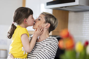 Mother and daughter kissing each other at home - WPEF07622