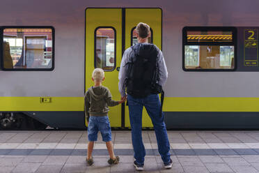 Vater und Sohn halten sich an den Händen und stehen vor einem Zug - NJAF00536
