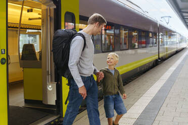 Glücklicher Sohn und Vater gehen auf dem Bahnsteig vor einem Zug - NJAF00538