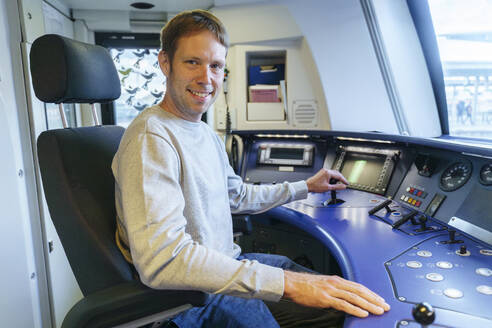 Glücklicher Mann sitzt im Cockpit einer Zuglokomotive - NJAF00542