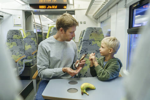 Vater und Sohn essen Banane im Zug - NJAF00546