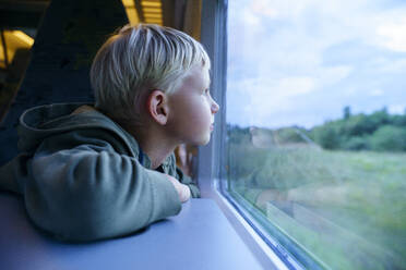 Contemplative blond boy looking through train window - NJAF00553