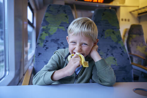 Glücklicher Junge isst Banane im Zug - NJAF00555