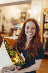 Happy redhead woman doing grocery shopping at store - KNSF09692