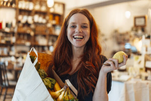 Happy redhead woman holding pear fruit and doing grocery shopping - KNSF09693