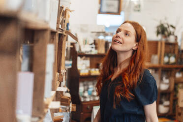 Lächelnde rothaarige Frau beim Einkaufen im Geschäft - KNSF09697