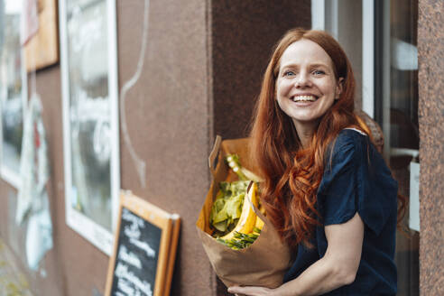 Happy redhead woman standing with bag of groceries outside store - KNSF09702